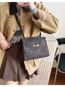 Detail view of charcoal leather shoulder bag with gold metal clasp on a stylish model