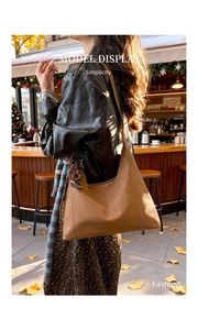 Detail of camel hobo bag with contrast stitching and branded charm in autumn setting