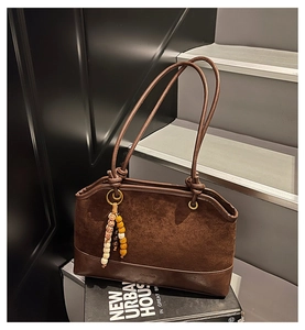Detail of dark brown suede tote bag with beaded charm on a minimalist staircase