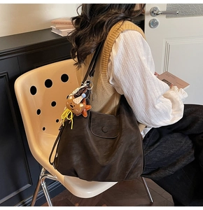 Detail of a large dark brown hobo tote bag in soft matte leather with a cute bear charm