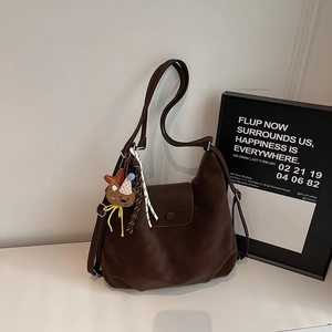 Close-up of dark brown soft leather hobo bag with bear charm and flip-top buckle detail