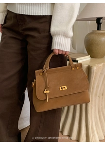 Close-up of brown suede handbag featuring a gold twist lock and vintage key charm