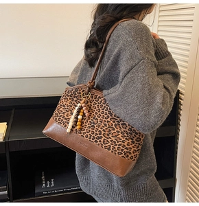 Detail view of large leopard print tote bag with brown leather trim and wood bead charm