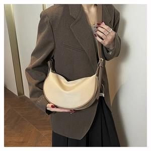 Close-up of beige lychee grain leather dumpling bag with brown trim and adjustable strap