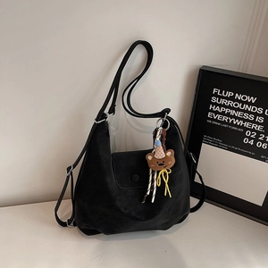 Detail of black matte leather tote bag with a cute brown bear charm on the side