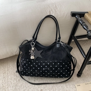 Dettaglio della borsa tote nera con texture scamosciata, motivo a pois e ciondolo a fiocco