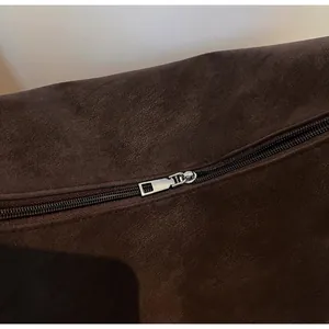 Detail des silbernen Reißverschlusses und der dunkelbraunen Wildlederoptik der Tasche