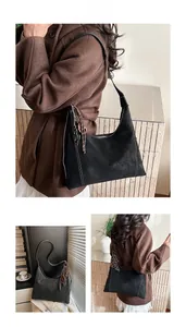 Detail view of black suede shoulder bag with wavy stitching and woven tassel pendant charm