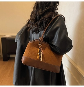 Detail of retro brown suede tote bag with leather patchwork and beaded tassel charm