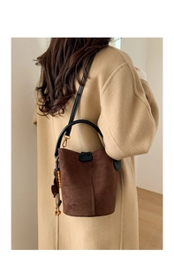 Detail of dark brown suede bucket bag with wooden bead tassel and black top handle