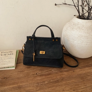 Detail of a vintage black matte handbag with gold lock, key pendant, and metal rivets