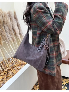 Detail of dark brown suede hobo bag with vintage metal charm and embossed texture