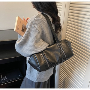 Fashionable black baguette bag with silver chain charms and zipper details worn by a model