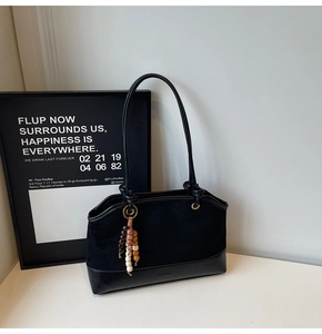 Detail of black suede tote bag with slim shoulder strap and stylish beaded tassel charm
