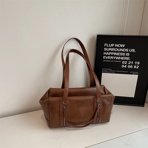 Detail view of brown faux leather shoulder bag with decorative zippers and rivets on marble