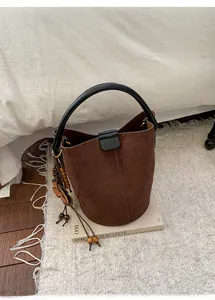 Detailed view of coffee suede bucket bag with leather strap and decorative floral pendant