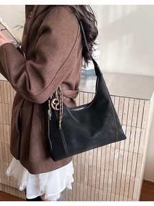 Detail of black suede tote bag with white contrast stitching and a knotted charm