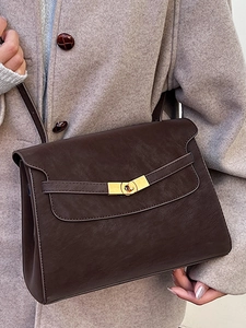 Classic dark brown leather crossbody bag with gold buckle on a stylish camel coat
