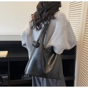 Side view of a large black leather tote bag worn by a model in a minimalist home setting