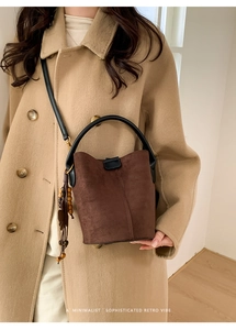 Detail of a dark brown suede bucket bag featuring wood bead tassel and black leather strap