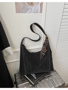 Detail of black suede tote bag with white contrast stitching and a brown charm on a silver case