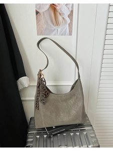 Detail of grey vintage tote bag with heart charm and tassels on a metal suitcase