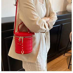 Detail of red quilted bucket bag with gold zipper shown on model in a beige suit