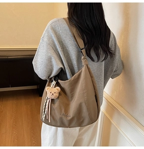 Detail view of large brown canvas tote bag with letter embroidery and cute plush bear charm