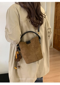 Detail of brown suede bucket bag with black leather handle and floral tassel accessory