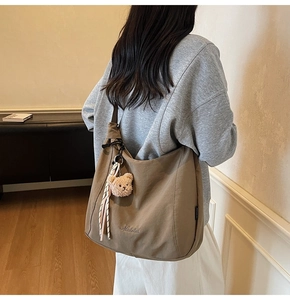 Detailed close-up of a brown canvas tote bag featuring embroidered lettering and a plush bear charm