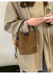 Detail of retro suede bucket bag with round handles and wooden bead tassels on a trench coat