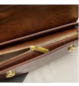 Close-up of smooth gold metal zipper and magnetic buckle on brown leather bag