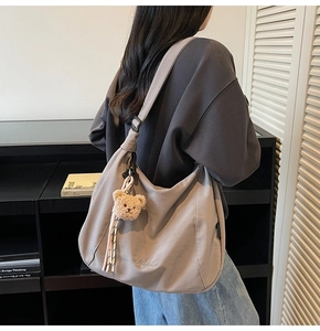 Detail of grey canvas hobo bag with letter embroidery and cute bear keychain charm