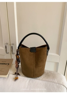 Detail of brown suede bucket bag with black handle and decorative floral wooden charm