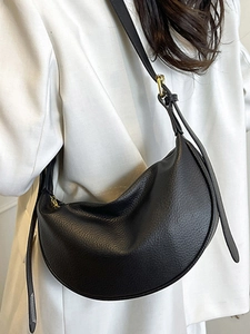 Minimalist black crescent shoulder bag in pebble leather with gold hardware on white blazer