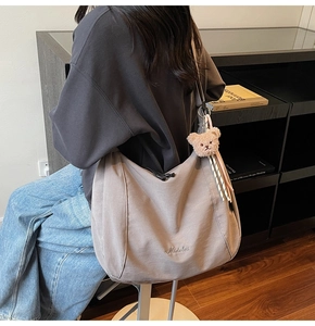 Detail view of large grey canvas tote bag with side bear charm on a female model