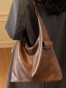 Large brown oily leather tote bag with knot strap detail worn by model in gray coat