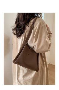 Brown litchi grain leather bucket bag shown from a side view with a beige trench coat