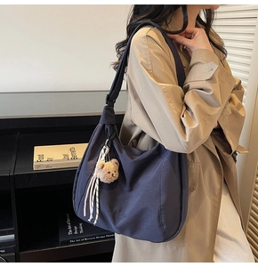 Detail of dark blue tote bag featuring a cute plush bear pendant and tassel accessory