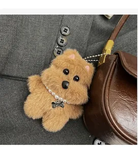 Plush brown dog charm with pearl necklace and bone tag on a leather handbag