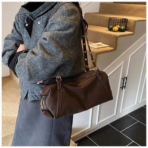 Detail of dark brown cylindrical Boston bag with adjustable strap and gold hardware