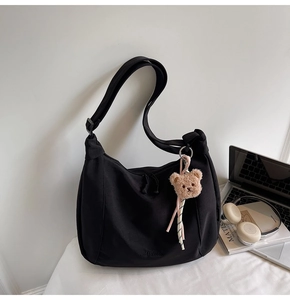 Close-up of black half-moon tote bag with brown bear charm and silk ribbon detail