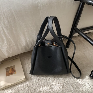 Detail of black pebbled leather bucket bag with gold hardware on a plush rug
