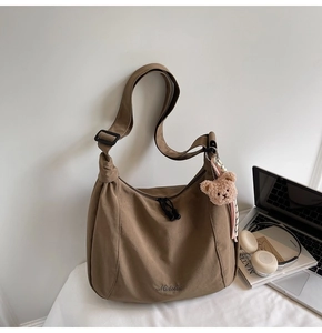 Detailed view of the large khaki tote bag with a plush bear charm and laptop