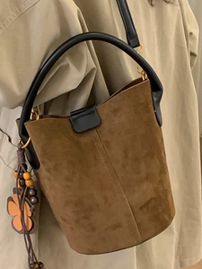 Retro dark brown suede bucket bag with leather handles shown on a khaki trench coat