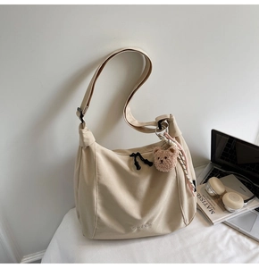 Detail view of a beige nylon shoulder bag with cute plush bear charm in a lifestyle setting