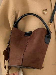 Retro dark brown suede bucket bag with black handles and wooden bead charm on a model