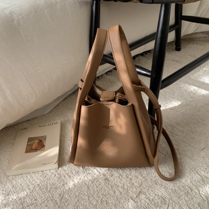 Detail of brown litchi pattern leather bucket bag with wide handles and logo in home setting