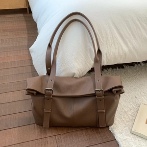 Close-up of brown pebbled leather tote bag with decorative adjustable metal buckle straps