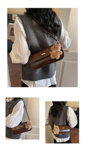 Detail of a brown leather shoulder bag with a cute plush bear and pearl charm accessory